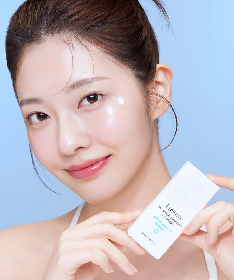 Décris l'image en français: LUVUM Bamboo Hyaluronic Acid Moisture Sunscreen 30ml, femme au selfie, tube à la main, fond bleu.