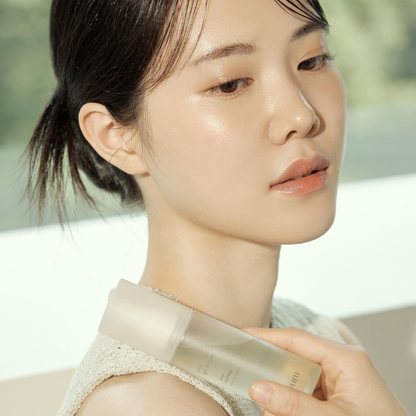 Décris l'image en français : LUVUM Calming Repair Cica Gel Serum 80ml, flacon posé sur une épaule, femme au naturel.