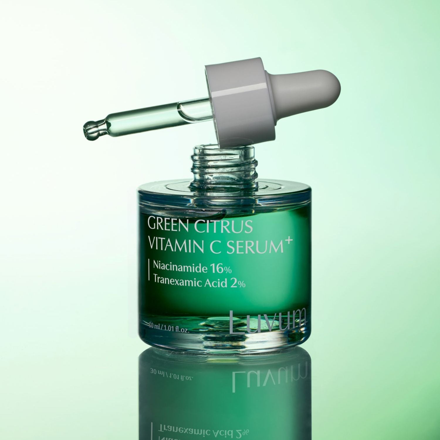 Décris l'image en français : LUVUM Green Citrus Vitamin C Serum Plus 30ml, flacon vert sur fond vert, goutte de sérum