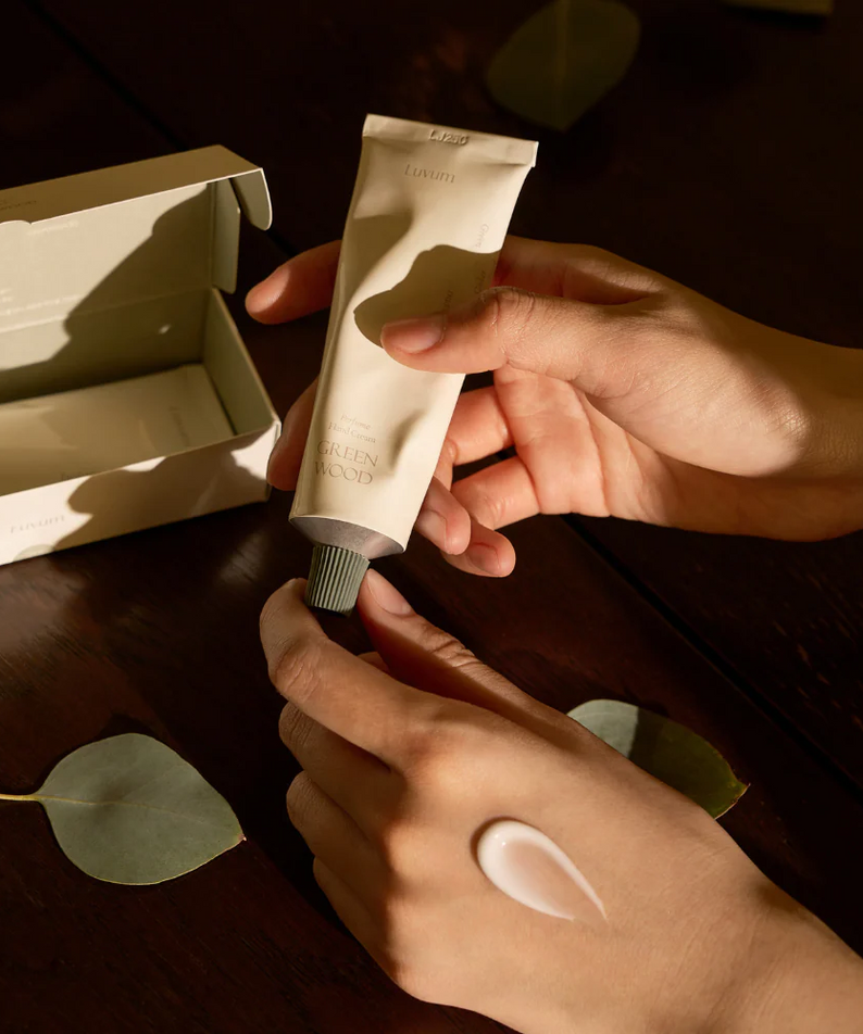 LUVUM Green Wood Perfume Hand Cream 50ml de la marque LUVUM, main appliquant la crème sur fond bois, déco feuilles vertes