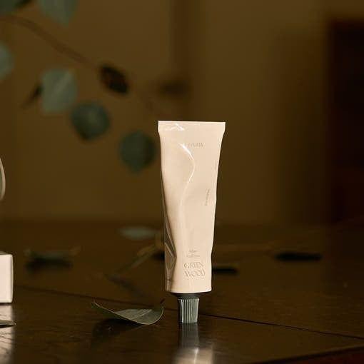 LUVUM Green Wood Perfume Hand Cream 50ml, main cream parfumée de la marque LUVUM sur table, décor feuilles vertes, flou arrière-plan.