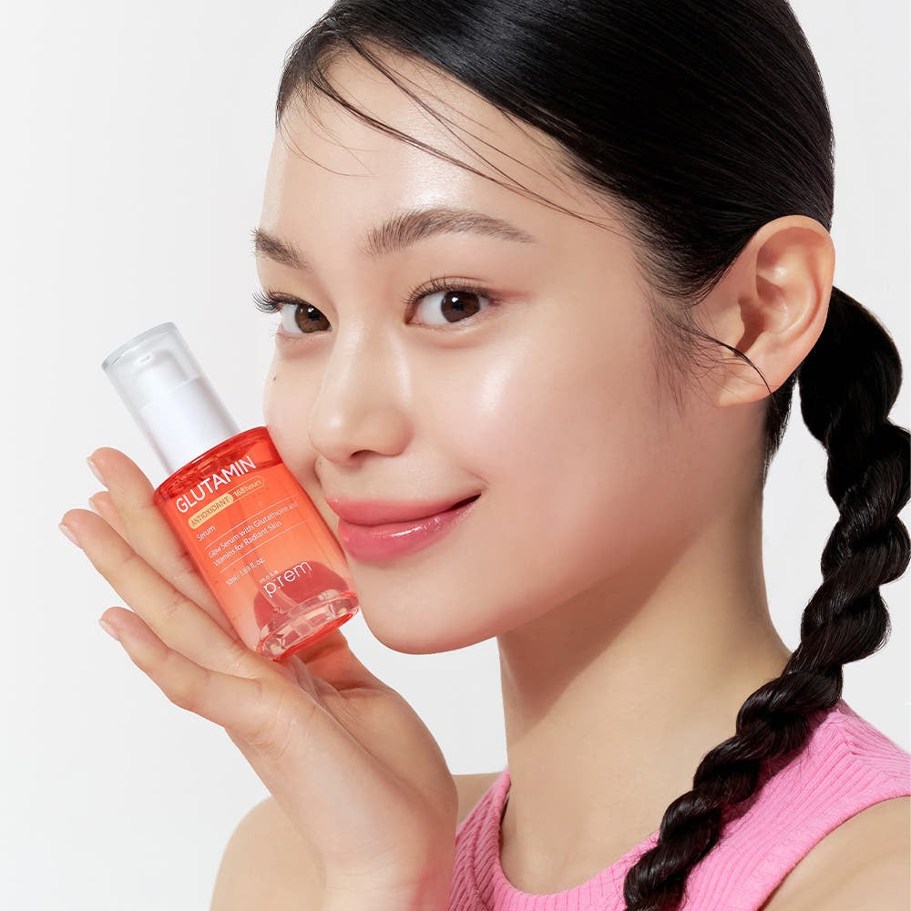 Décris l'image en français : MAKE P:REM Glutamine Antioxidant Radiance Serum 50ml, femme tenant le flacon sur fond blanc