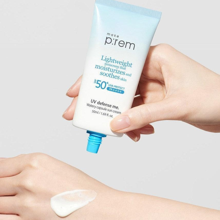 MAKE P:REM  UV Defense Me Watery Capsule Sunscreen 50ml SPF50+ PA++++, main tenant le tube bleu sur peau, fond clair.