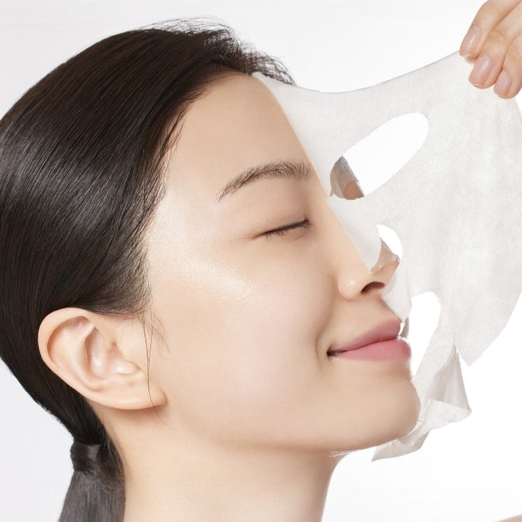 MAMONDE Age Control Camellia Ampoule Mask Pack: femme applique un masque en tissu camélia, soin anti-âge en gros plan.
