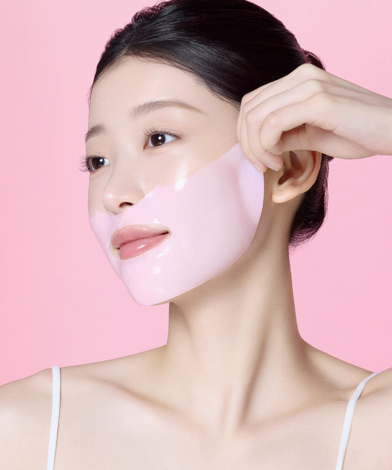 MAMONDE Flora Glow Rose Hydrogel Mask 1 sheet, marque MAMONDE : masque rose en gel sur visage, main pose la feuille, fond rose.