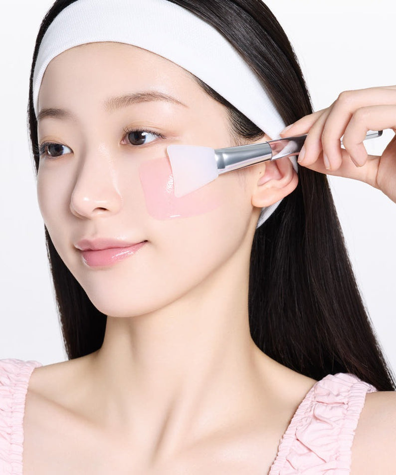 MAMONDE Flora Glow Rose Sleeping Mask 80ml, femme applique une crème rosée au pinceau sur le visage, fond blanc.