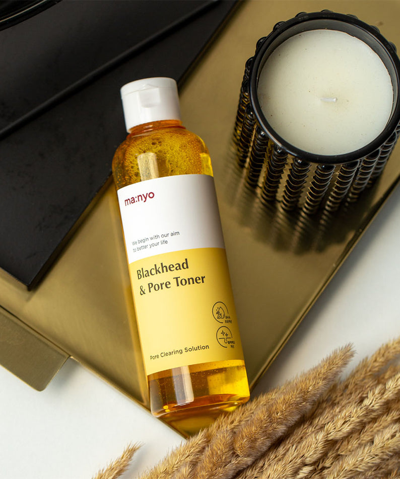 MANYO Blackhead & Pore Toner 210ml sur une table dorée avec une bougie noire, produit de soin pour les pores et points noirs.