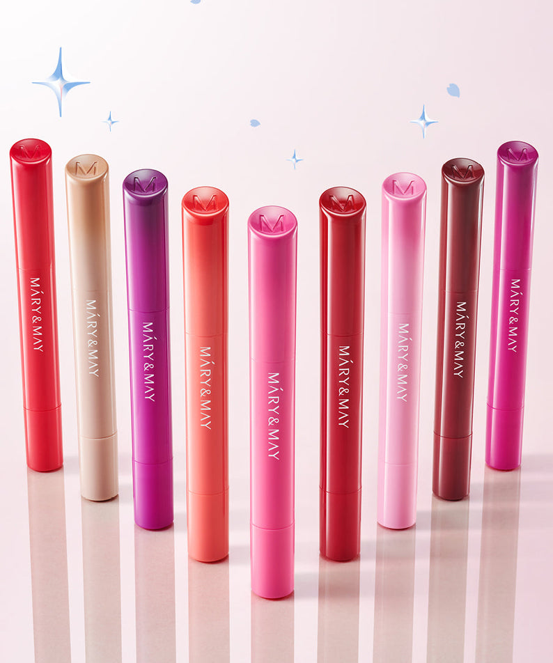 MARY&MAY Blooming Glow Lip 09 Sunset Tangerine 1.7g, sur fond rose avec plusieurs baumes de la marque, étoiles décoratives.