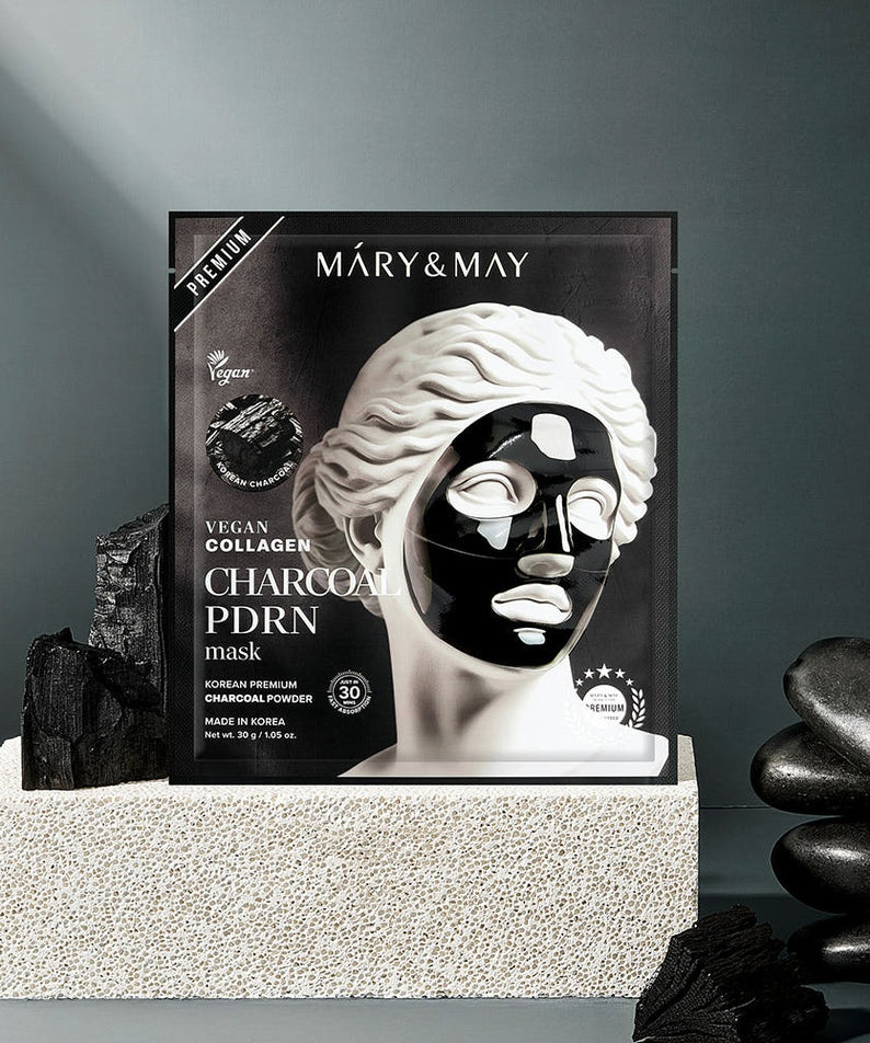 MARY&MAY Vegan Collagen Charcoal PDRN Gel Mask (4 Sheets) sur un socle avec des pierres noires, masque visage élégant en arrière-plan.