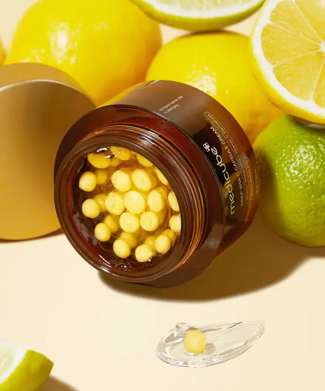 Crème MEDICUBE Deep Vita C Capsule 55g avec capsules vitaminées, entourée de citrons et limes pour un soin éclatant et lumineux.