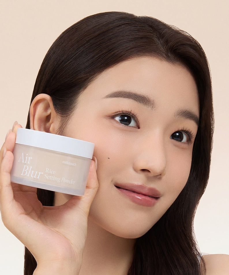 MILK TOUCH Air Blur Rice Setting Powder de la marque sur une femme, pot tenu en gros plan, peau floutée, studio