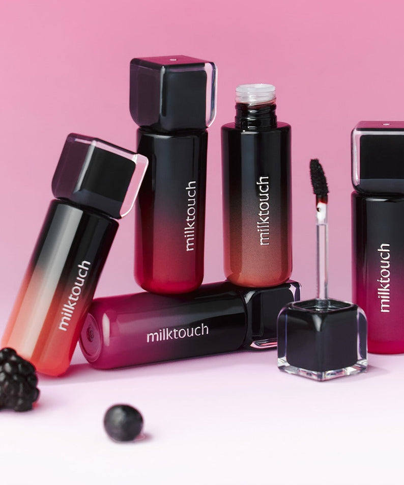 Décris l'image en français : MILK TOUCH Black Peel-Off Lip Tattoo, flacons et applicateur maquillage sur fond rose.