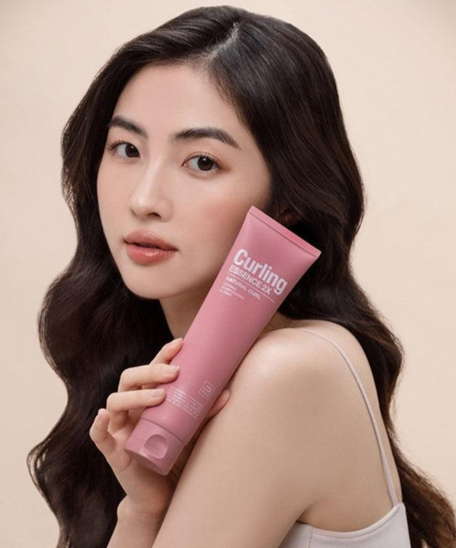 Portrait femme tenant MISE EN SCENE Curling Essence 2X 150ml, tube rose sur fond clair, marque MISE EN SCENE.