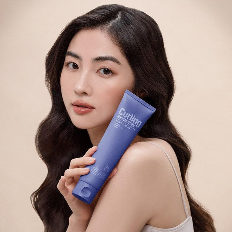 MISE EN SCENE Curling Essence 2X 150ml : tube bleu tenu par une femme aux cheveux bouclés, fond beige, branding visible.