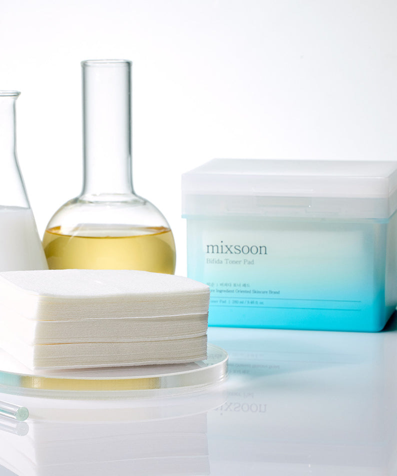 MIXSOON Bifida Toner Pad en scène avec des flacons laboratoires, présentation élégante pour soins de la peau.