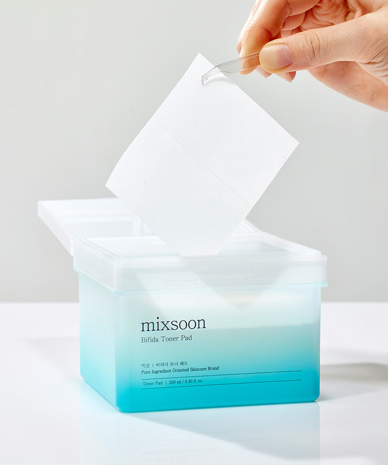 MIXSOON Bifida Toner Pad en cours d'utilisation avec une main qui sort un pad de la boîte ouverte, soins de la peau efficaces MIXSOON.