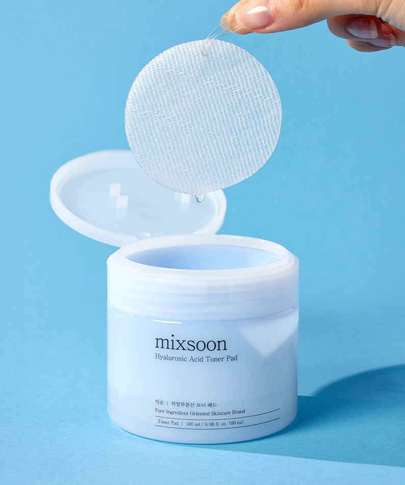 MIXSOON Hyaluronic Acid Toner Pad sur fond bleu, main tenant un disque tonifiant.