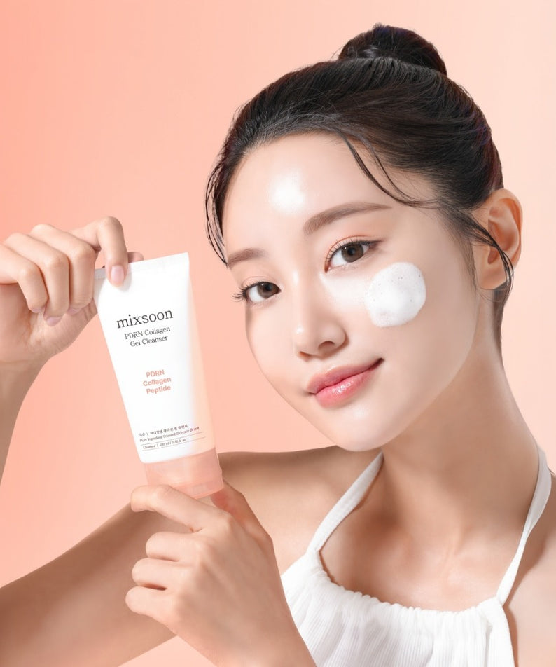 Femme souriante tenant MIXSOON PDRN Collagen Gel Cleanser 100ml avec mousse blanche sur la joue, fond pêche.