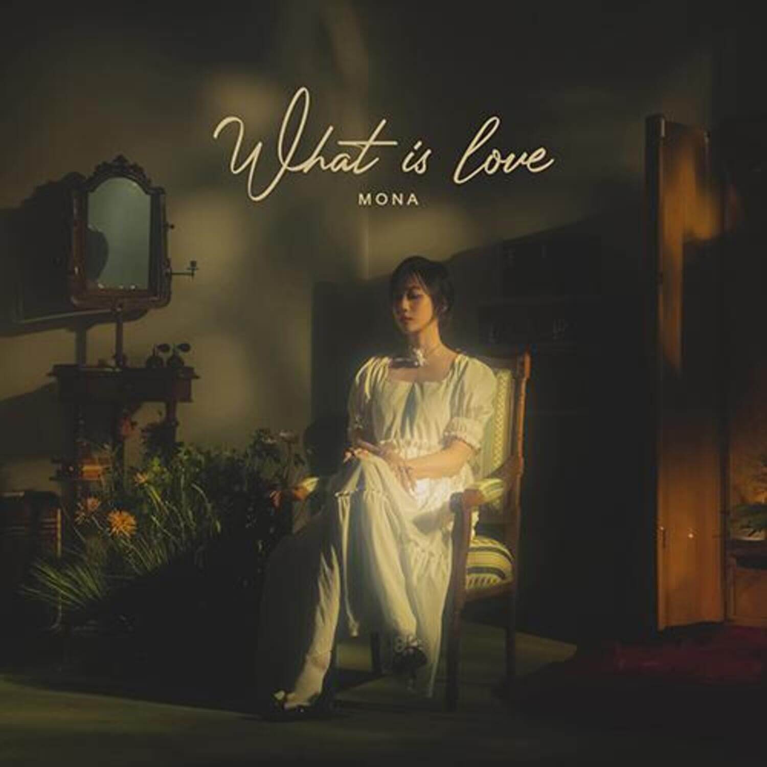 MONA - [What Is love] - Album Kpop : couverture sombre, artiste en robe blanche assise, studio rétro, fleurs et lumière chaude.