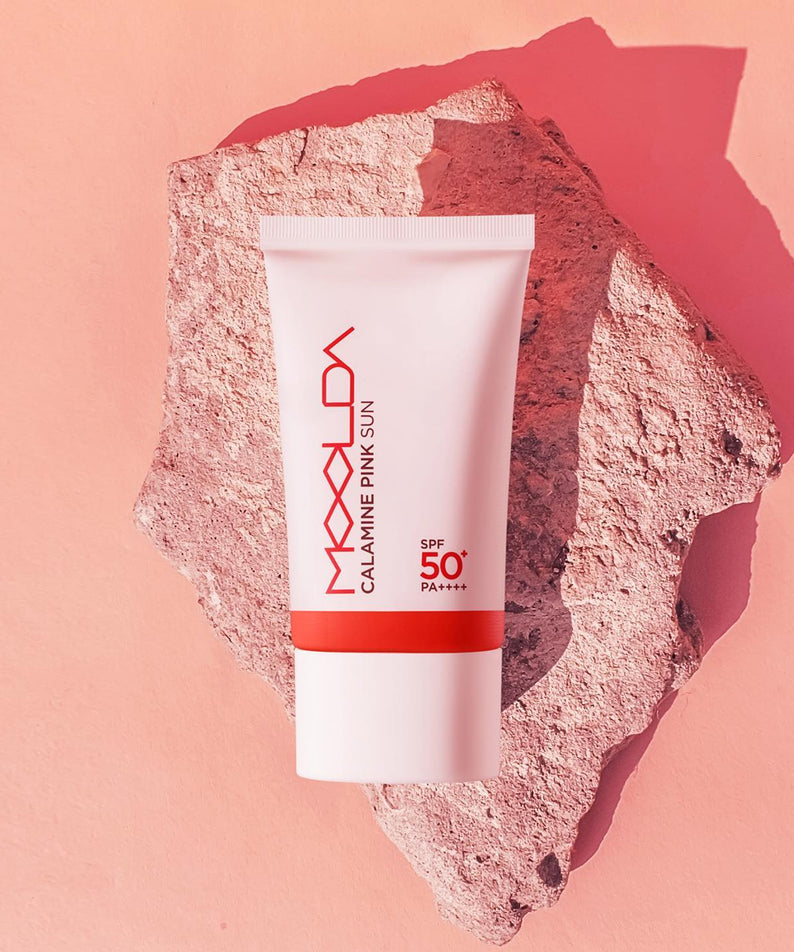 Crème solaire MOOLDA Calamine Pink Sun SPF50+ PA++++ sur fond rocheux rose.