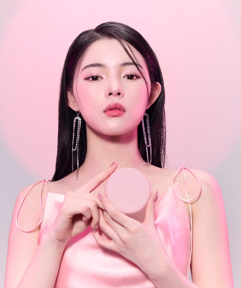Décris l'image en français : MOONSHOT Conscious Fit Cushion Foundation Pink Moon Edition, sur un packaging rond rose, peau lumineuse.