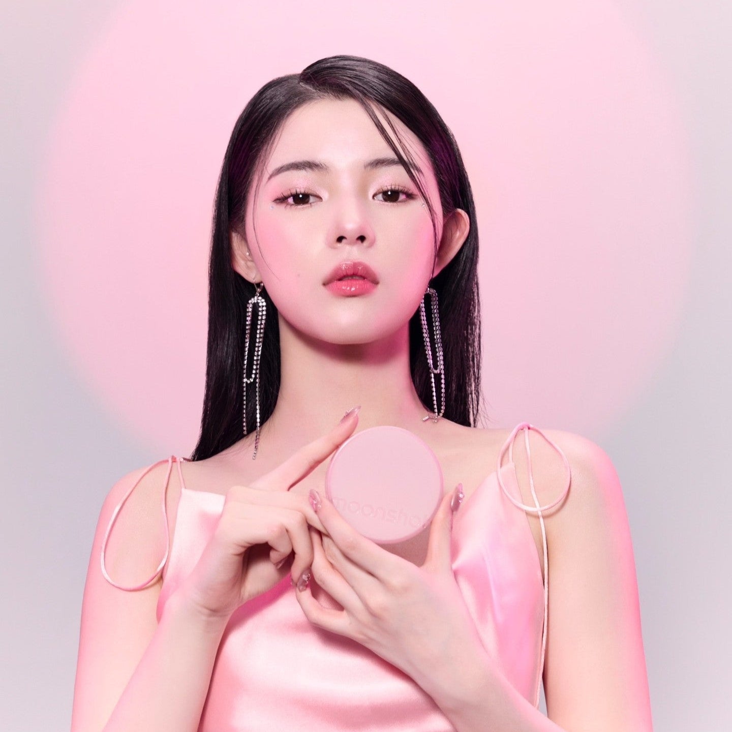 Décris l'image en français : MOONSHOT Conscious Fit Cushion Foundation Pink Moon Edition, sur un packaging rond rose, peau lumineuse.