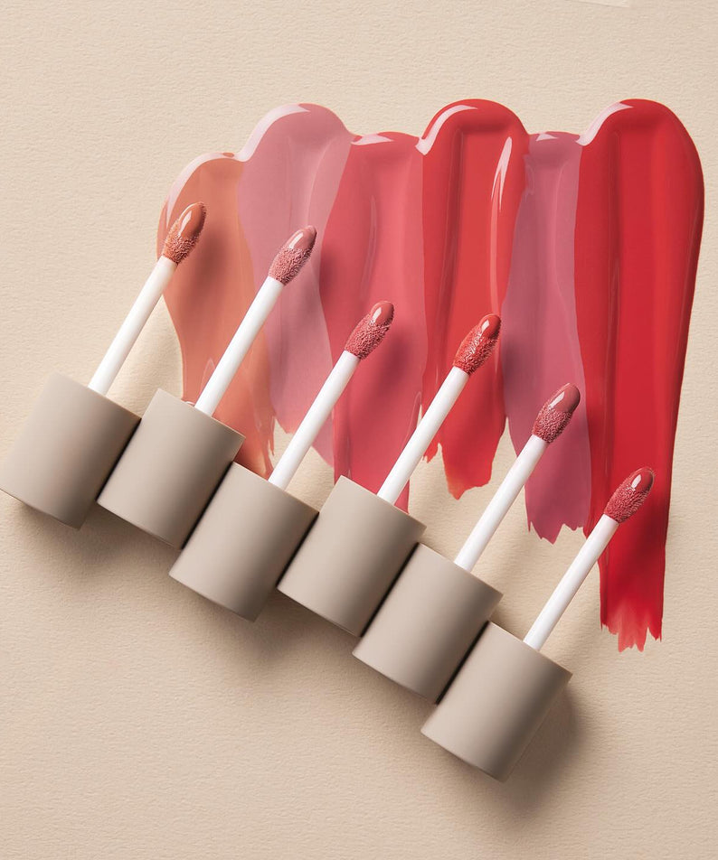 Différentes teintes de MOONSHOT Conscious Fit Melow Lip Tint sur un fond beige, mettant en valeur la variété des couleurs disponibles.