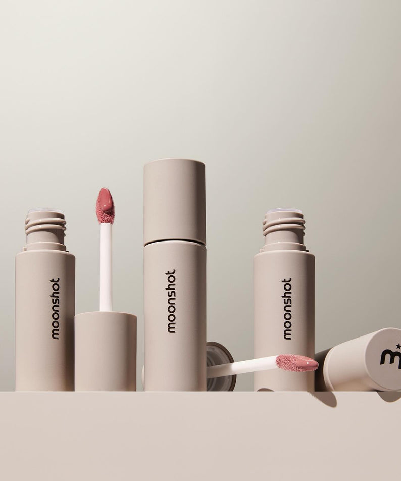 MOONSHOT Conscious Fit Melow Lip Tint, élégante collection de tubes beige avec applicateur rose, posée sur fond neutre minimaliste.