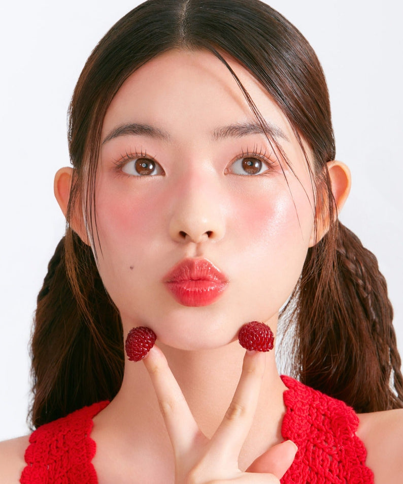 Femme portant MOONSHOT Melting Mood Lip & Cheek, avec un effet lèvres et joues rosées et des framboises comme décoration.