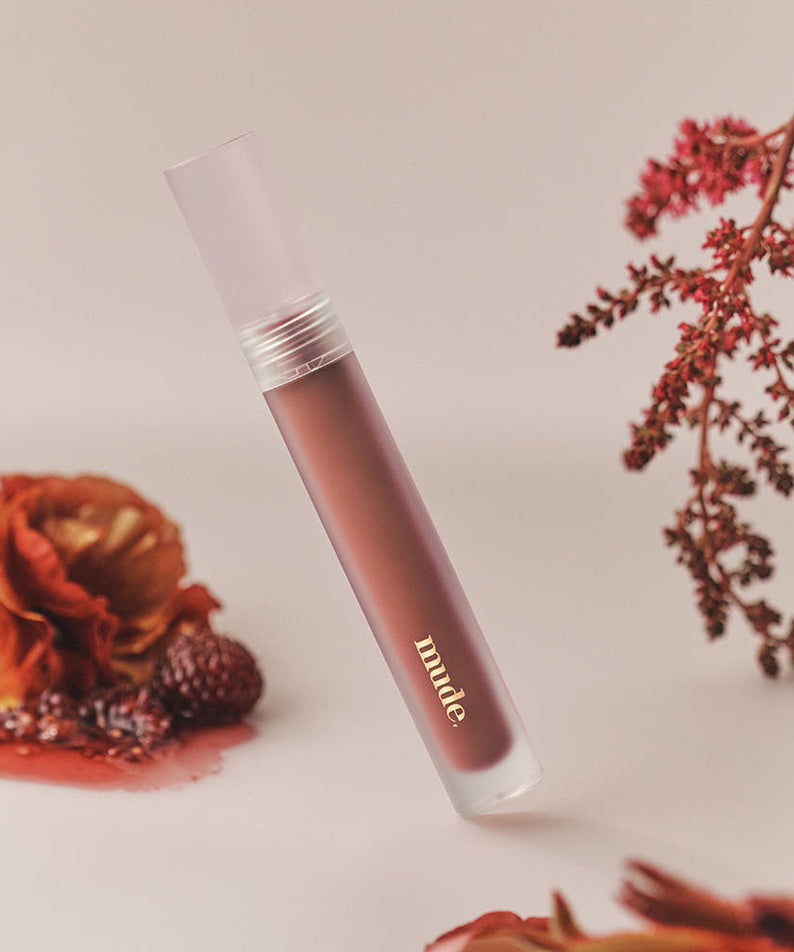 Mude Mood Soft Blur Tint, tube maquillage de la marque Mude, flou doux sur fond beige avec fleurs séchées.