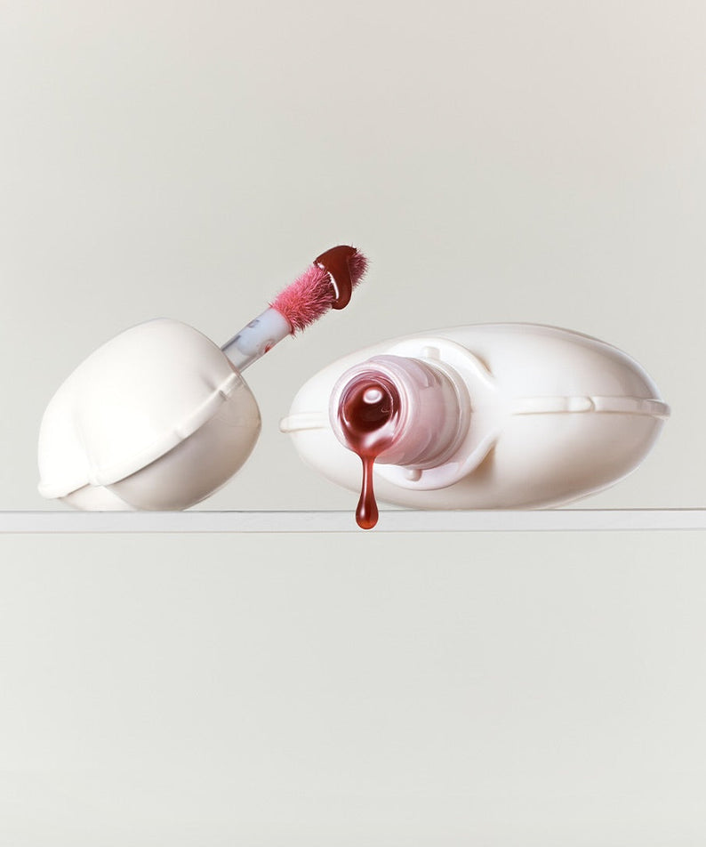 NAMING Glow Heart Lip Tint, flacon et applicateur sur fond clair, finition brillante, maquillage lèvres.