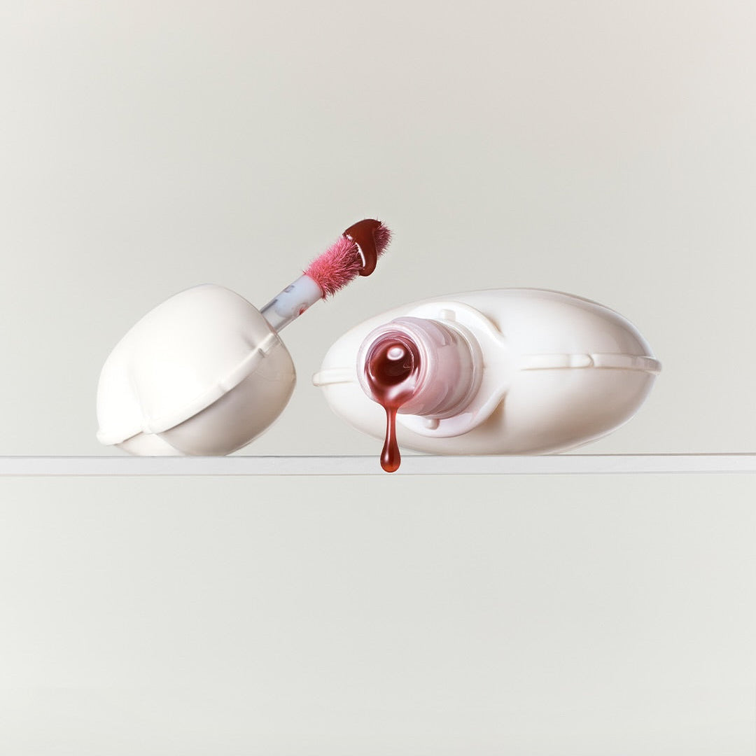 NAMING Glow Heart Lip Tint, flacon et applicateur sur fond clair, finition brillante, maquillage lèvres.