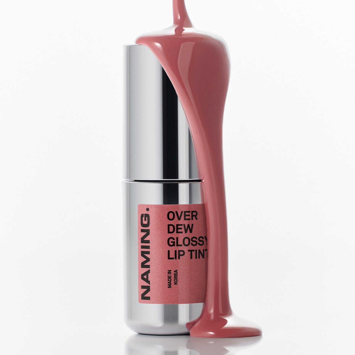 NAMING Overdew Glossy Lip Tint, tube argenté avec embout, reflet luisant sur fond blanc, maquillage lèvres.