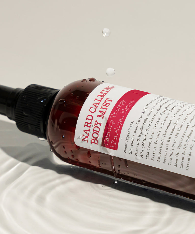 NARD Calming Body Mist 200ml : brume apaisante NARD sur tissu clair, flacon pulvérisateur, contexte beauté spa.