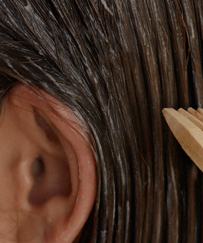 NARD Hair Treatment 1000ml, flacon de marque NARD, posé sur cheveux foncés et peigne en bois, contexte salon.