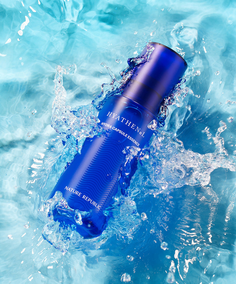 Flacon de NATURE REPUBLIC Hyathenol Hydra Capsule Essence 50ml sur fond d'eau éclaboussant.