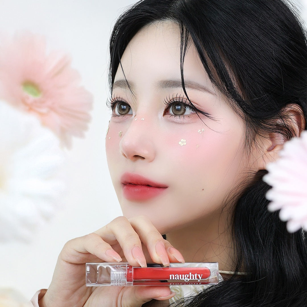 NAUGHTY PERCENT Matte Bloom Tint de la marque NAUGHTY PERCENT, maquillage mat sur modèle devant fleurs, flacon rouge en gros plan.
