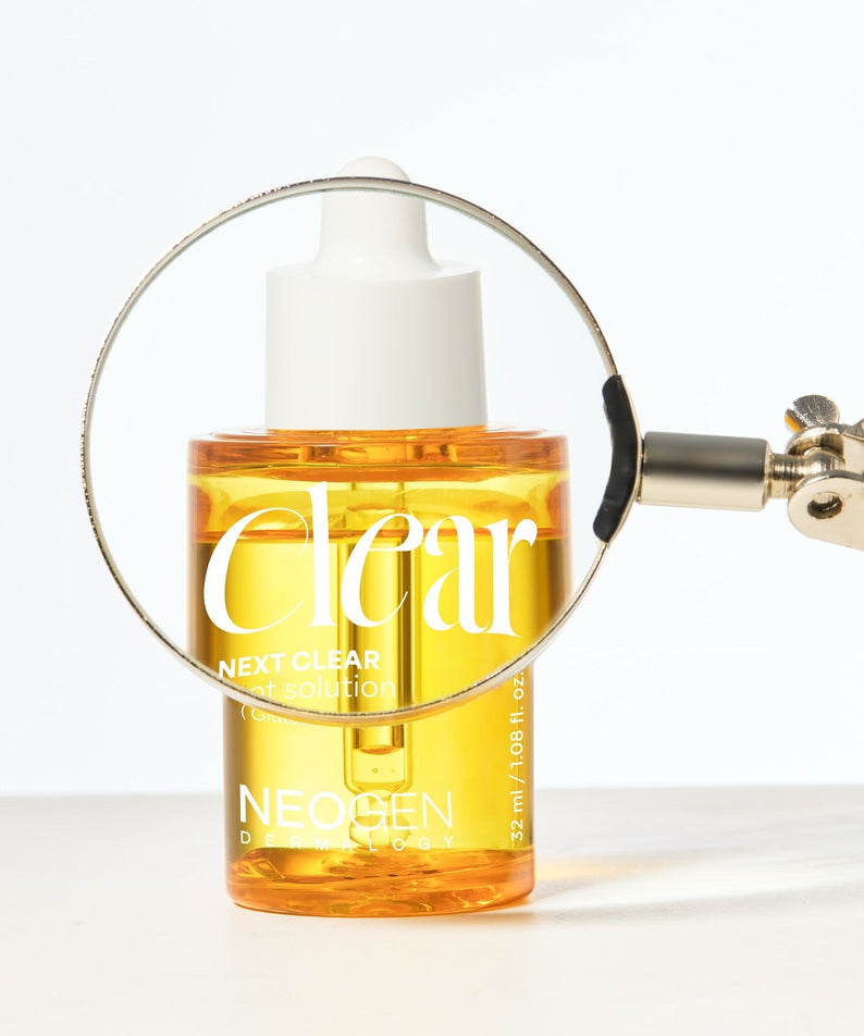 NEOGEN  Next Clear Spot Solution 32ml, flacon jaune avec loupe sur fond clair : soin anti-imperfections.