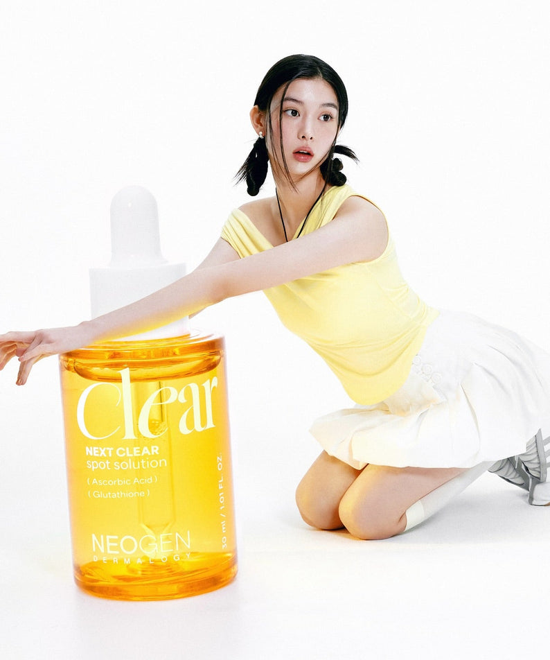 NEOGEN  Next Clear Spot Solution 32ml de Neogen, flacon jaune sur fond blanc avec une femme en séance soin visage.