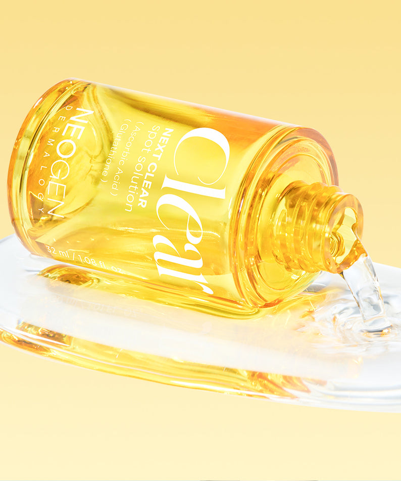 Flacon en verre de NEOGEN Next Clear Spot Solution 32ml versant son contenu liquide sur une surface blanche, fond jaune lumineux.