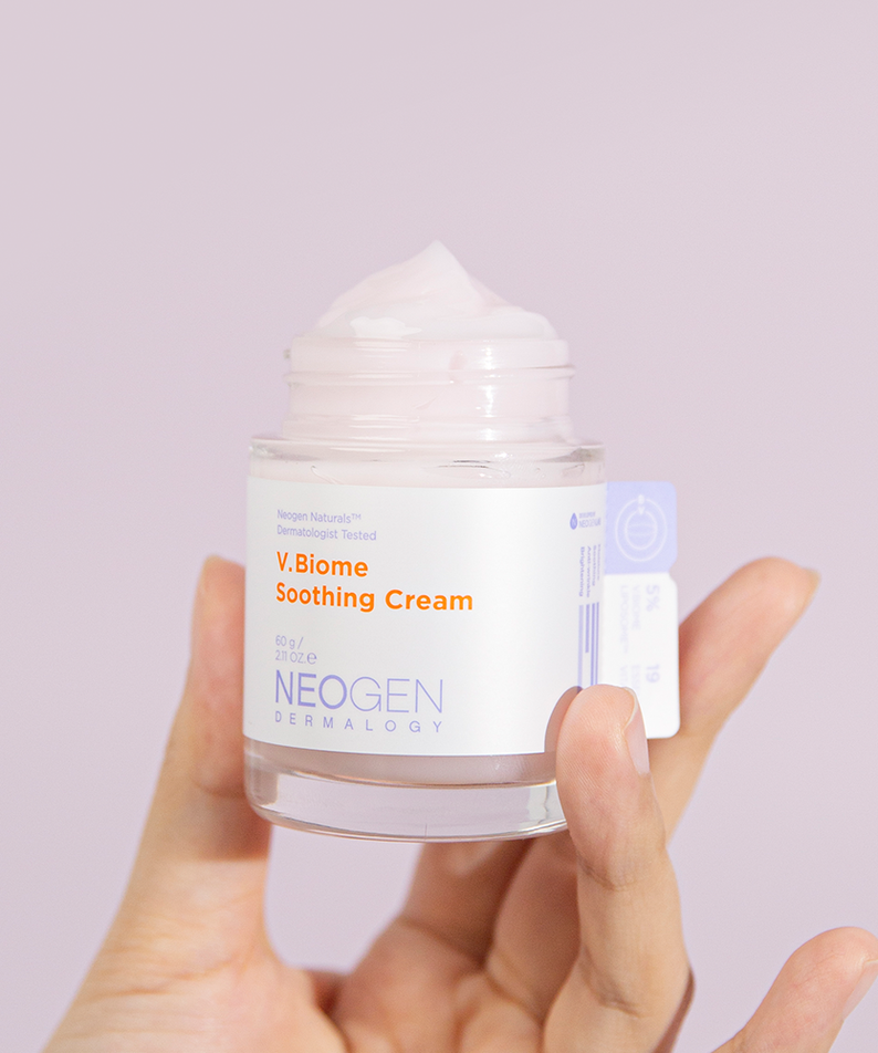 Pot de crème apaisante NEOGEN V Biome Soothing Cream 60g, tenu en main, sur fond rose pastel.