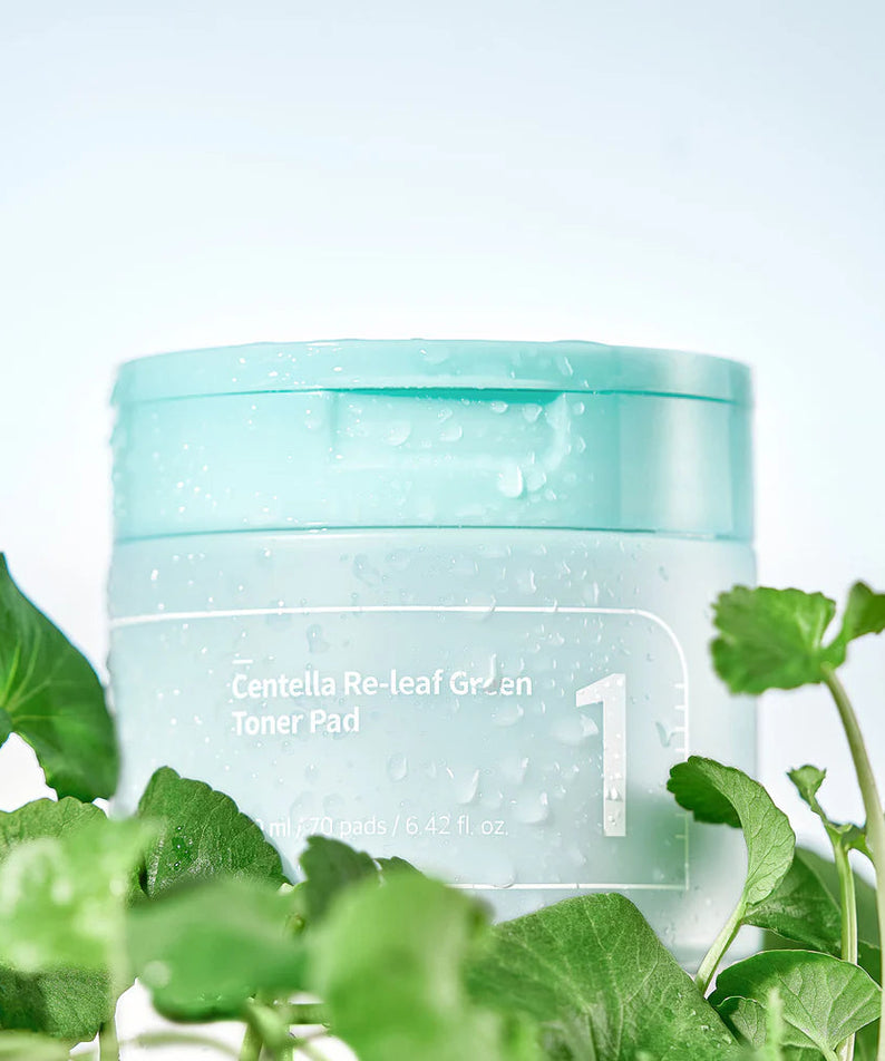 Boîte de NUMBUZIN No.1 Centella Re-Leaf Green Toner Pad entourée de feuilles vertes pour soin du visage.
