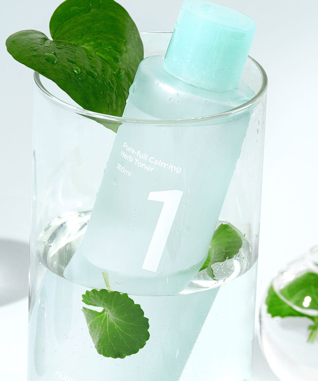 NUMBUZIN No.1 Pure-Full Calming Herb Toner dans un verre avec des feuilles, produit apaisant pour la peau. Flacon de tonique 30ml.