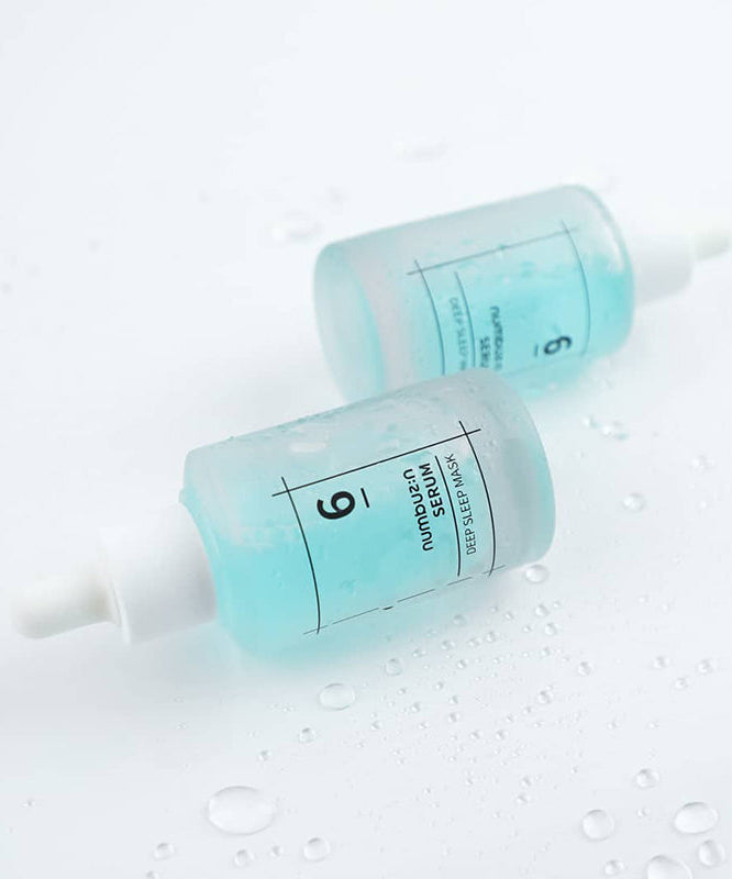 Deux flacons de NUMBUZIN No.6 Deep Sleep Mask Serum avec sérum bleu sur fond blanc avec gouttelettes d'eau.