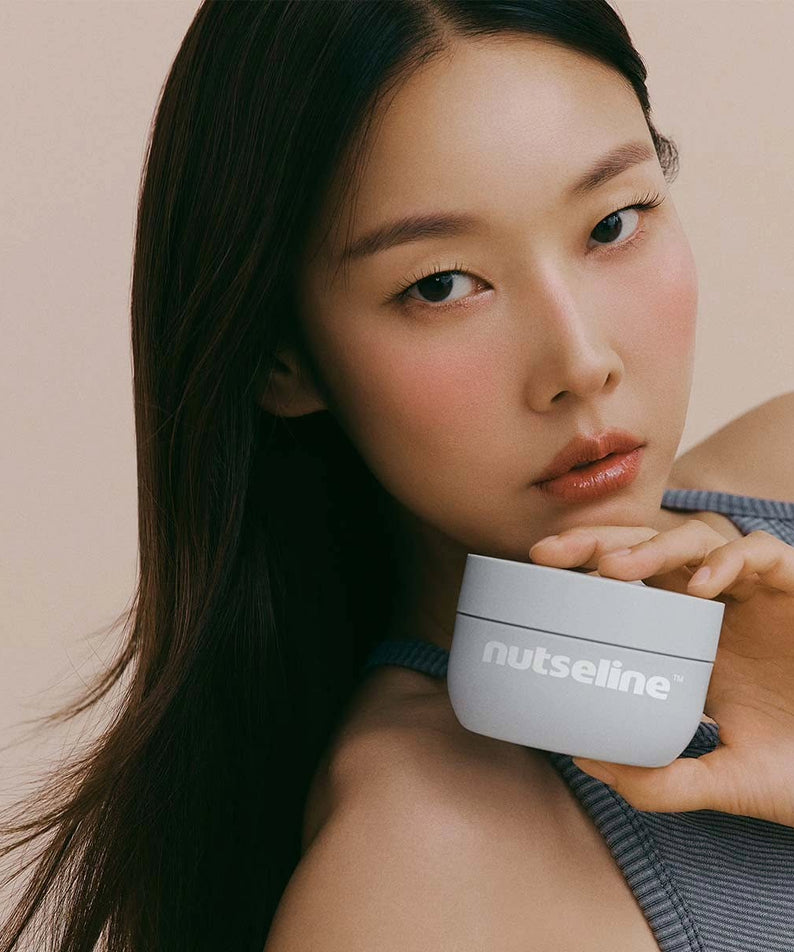 Femme posant avec NUTSELINE Aroma Nut Gray Body Scrub 200g, soin exfoliant en pot gris.