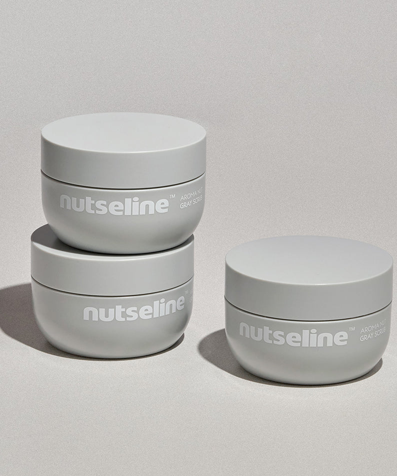 Trois pots de NUTSELINE Aroma Nut Gray Body Scrub 200g sur une surface grise, mise en avant du soin corporel exfoliant.