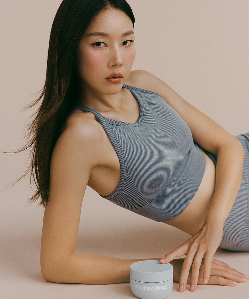 Femme posant avec NUTSELINE Aroma Nut Gray Body Scrub 200g, tenue grise assortie, ambiance détente.