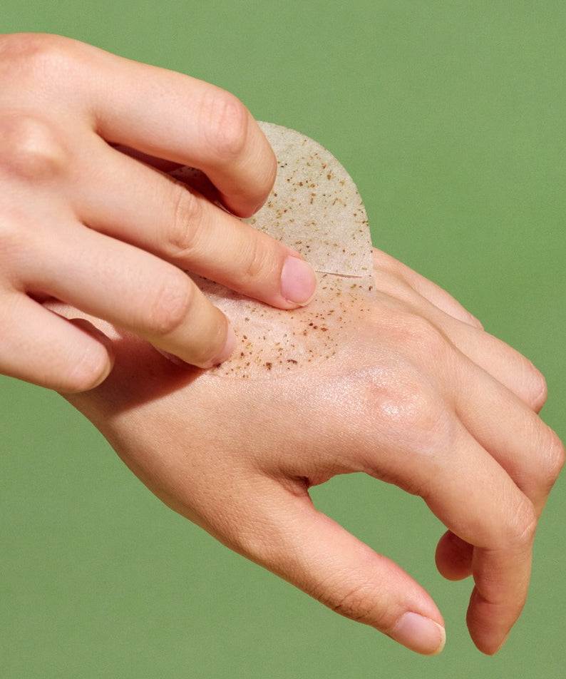 Main appliquant NUTSELINE Cica Calming Pad sur la peau, produit de la marque NUTSELINE, fond vert apaisant.