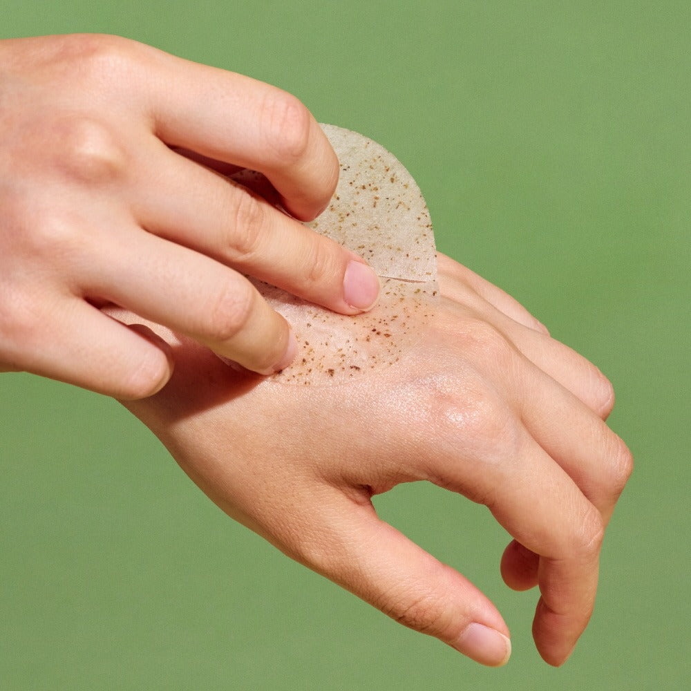 Main appliquant NUTSELINE Cica Calming Pad sur la peau, produit de la marque NUTSELINE, fond vert apaisant.