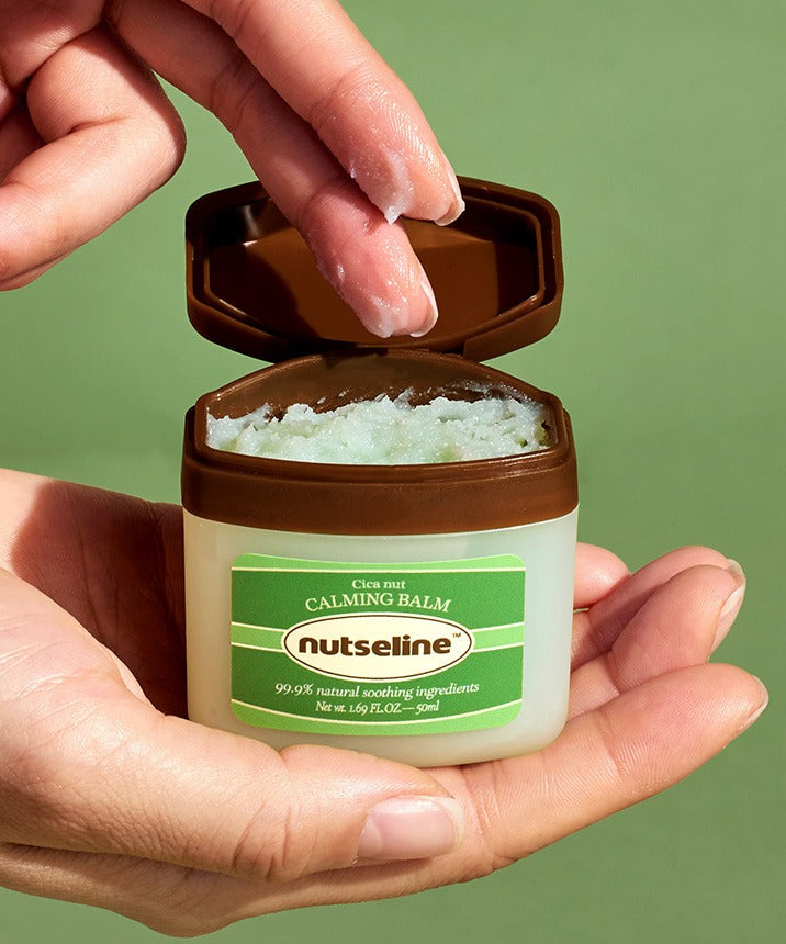 NUTSELINE Cica Nut Calming Balm Season 2 50ml : pot ouvert avec baume, mains, fond vert, contexte soins visage.